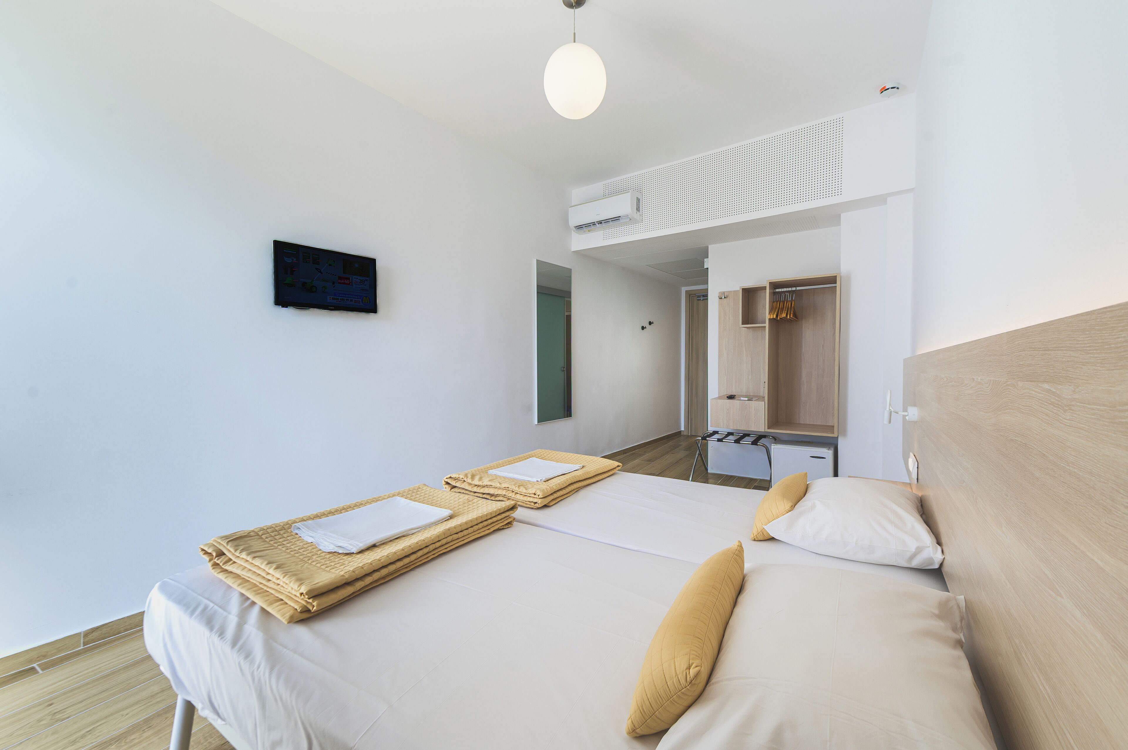 A hotel room with a bed, a wardrobe, a mirror, and a wall-mounted television.