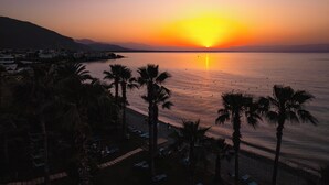 A beach with palm trees and a sunset. - Hotel Sissy (Kamena Vourla)