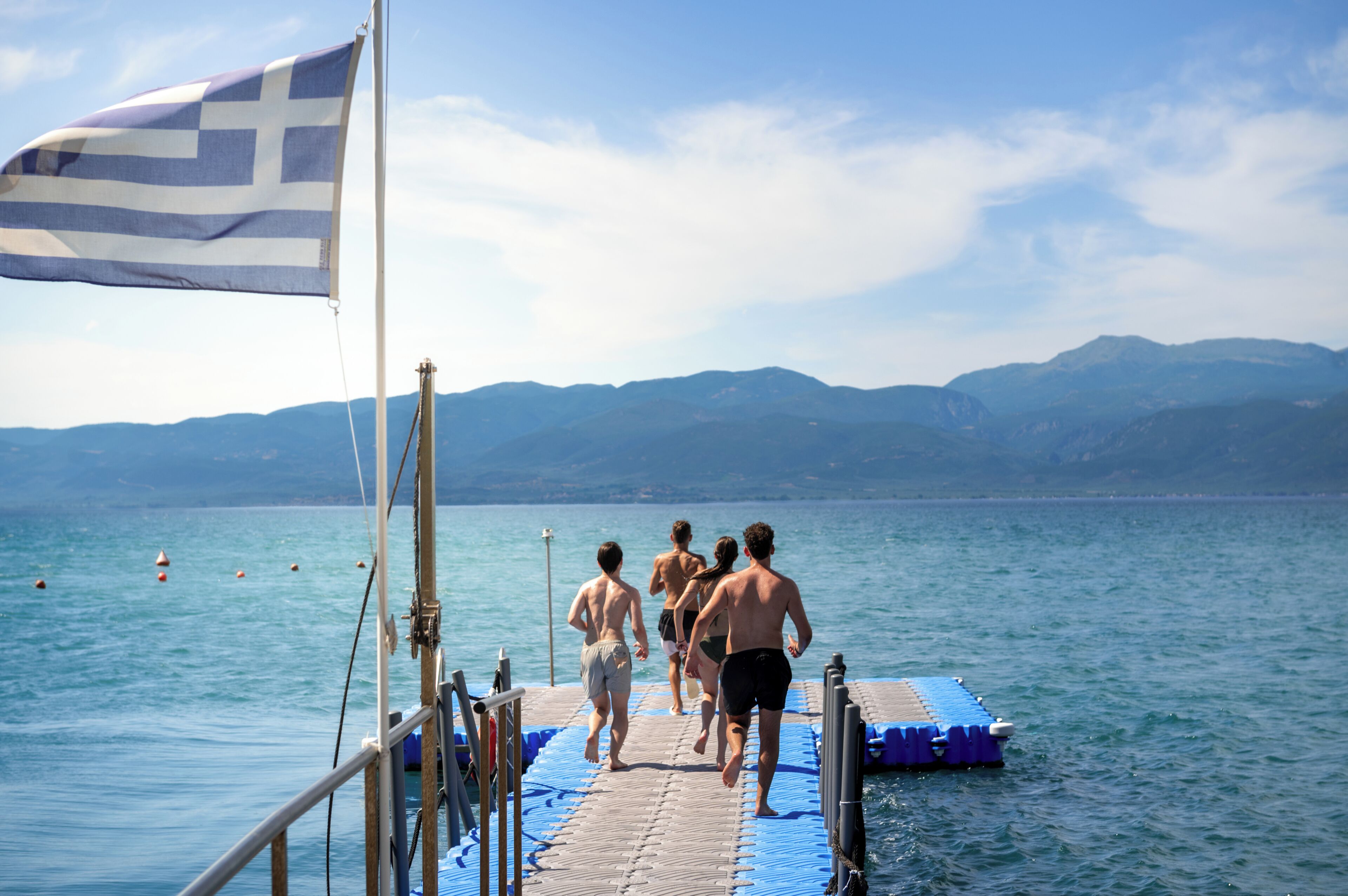 A group of people walking on a dock towards a body of water with mountains in the background.