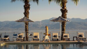 A poolside area with lounge chairs and umbrellas, overlooking a mountainous landscape. - Hotel Sissy (Kamena Vourla)