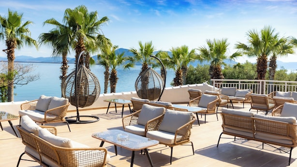 An outdoor seating area with wicker furniture and a view of the sea. - Hotel Sissy (Kamena Vourla)