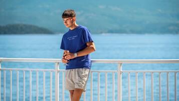 A person standing on a balcony with a railing, overlooking a body of water and a mountainous landscape.