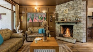 A cozy living room with a stone fireplace, patterned sofas, and a painting of flamingos. - The Bear Creek Homestay Manali (Manali)