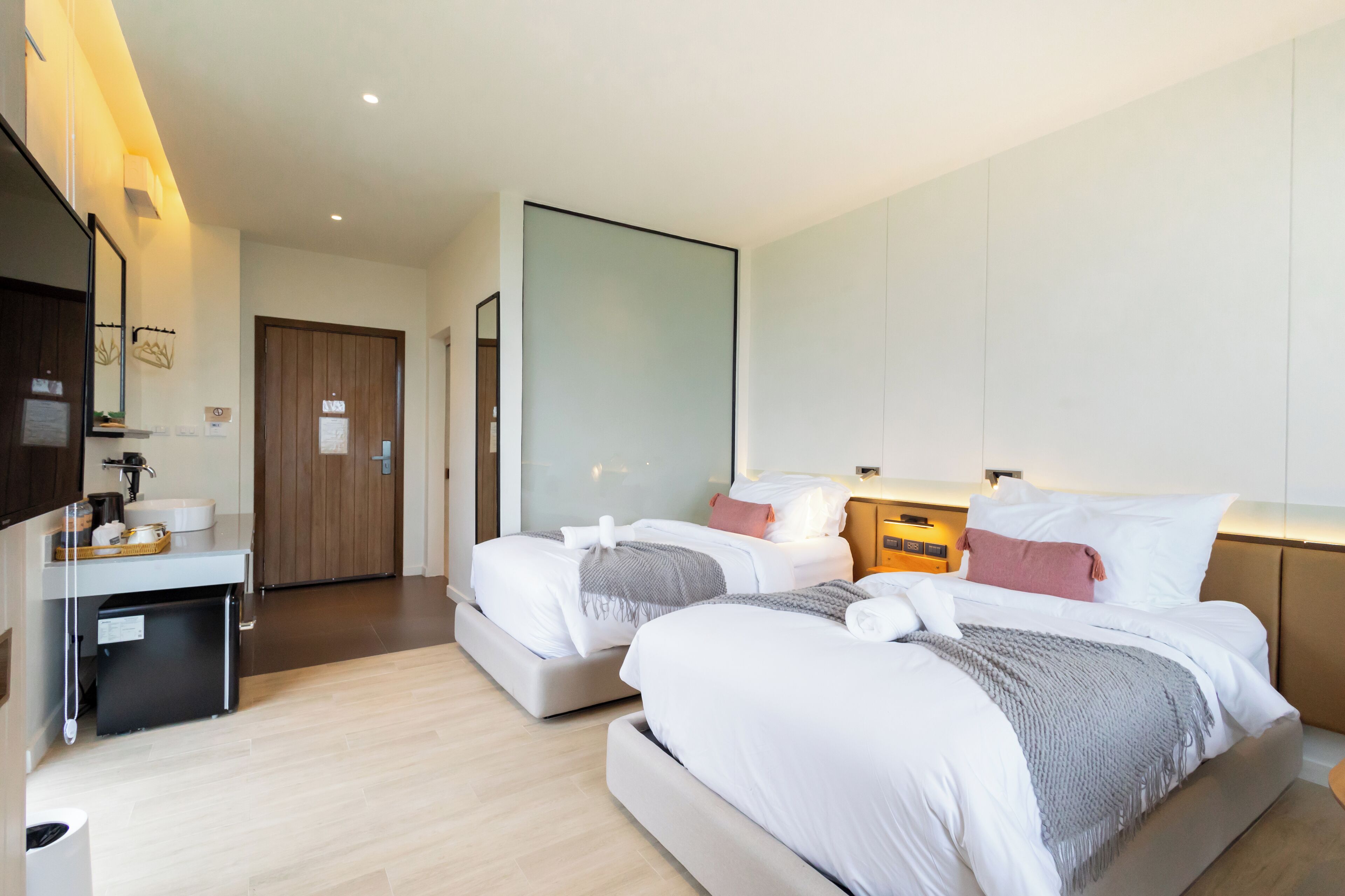 Una habitación de hotel moderna con dos camas, un pequeño escritorio con lavamanos y un espejo grande.