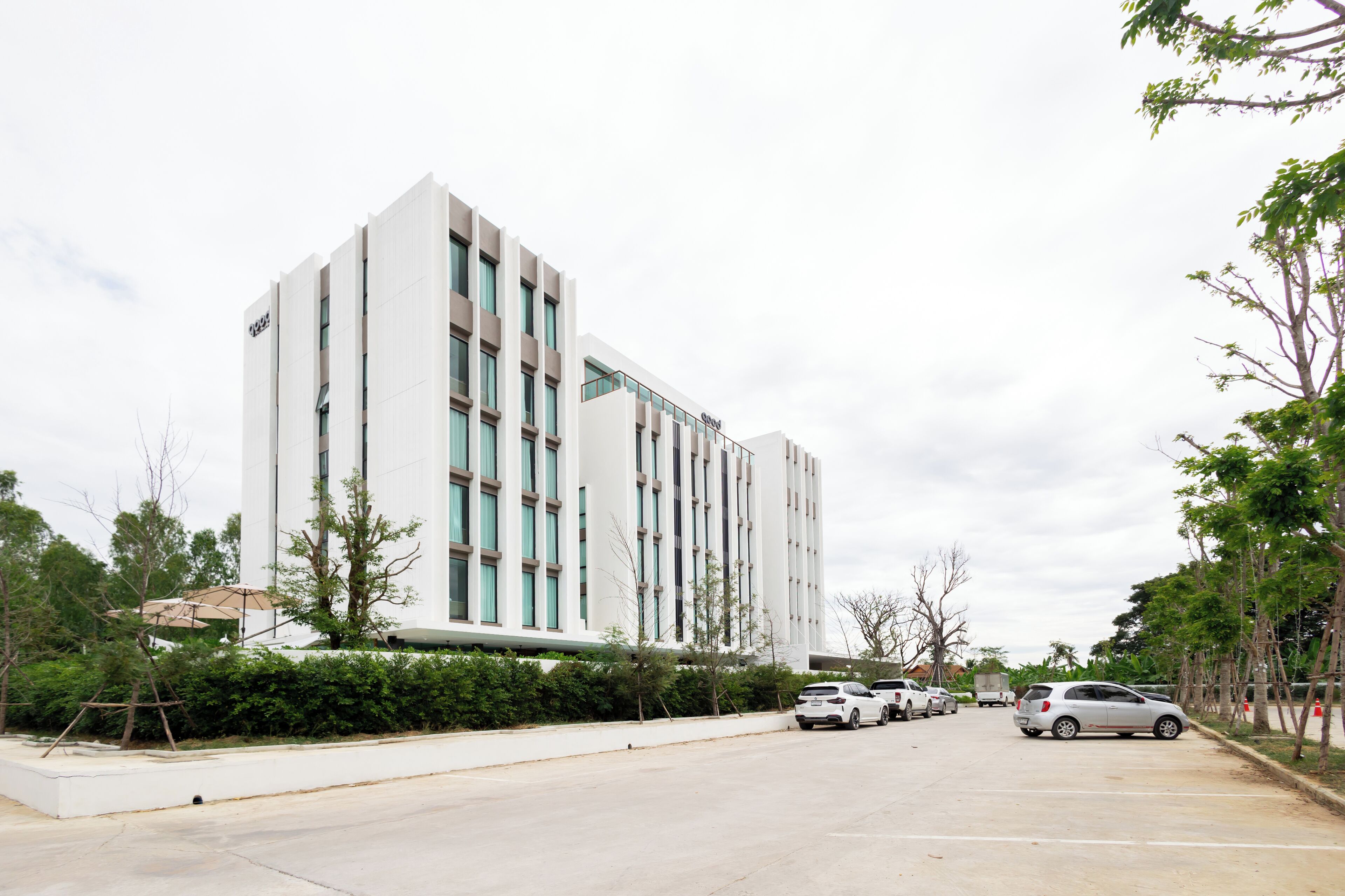 Un edificio moderno con fachada blanca y múltiples ventanas. Varias automóviles están estacionadas frente al edificio.