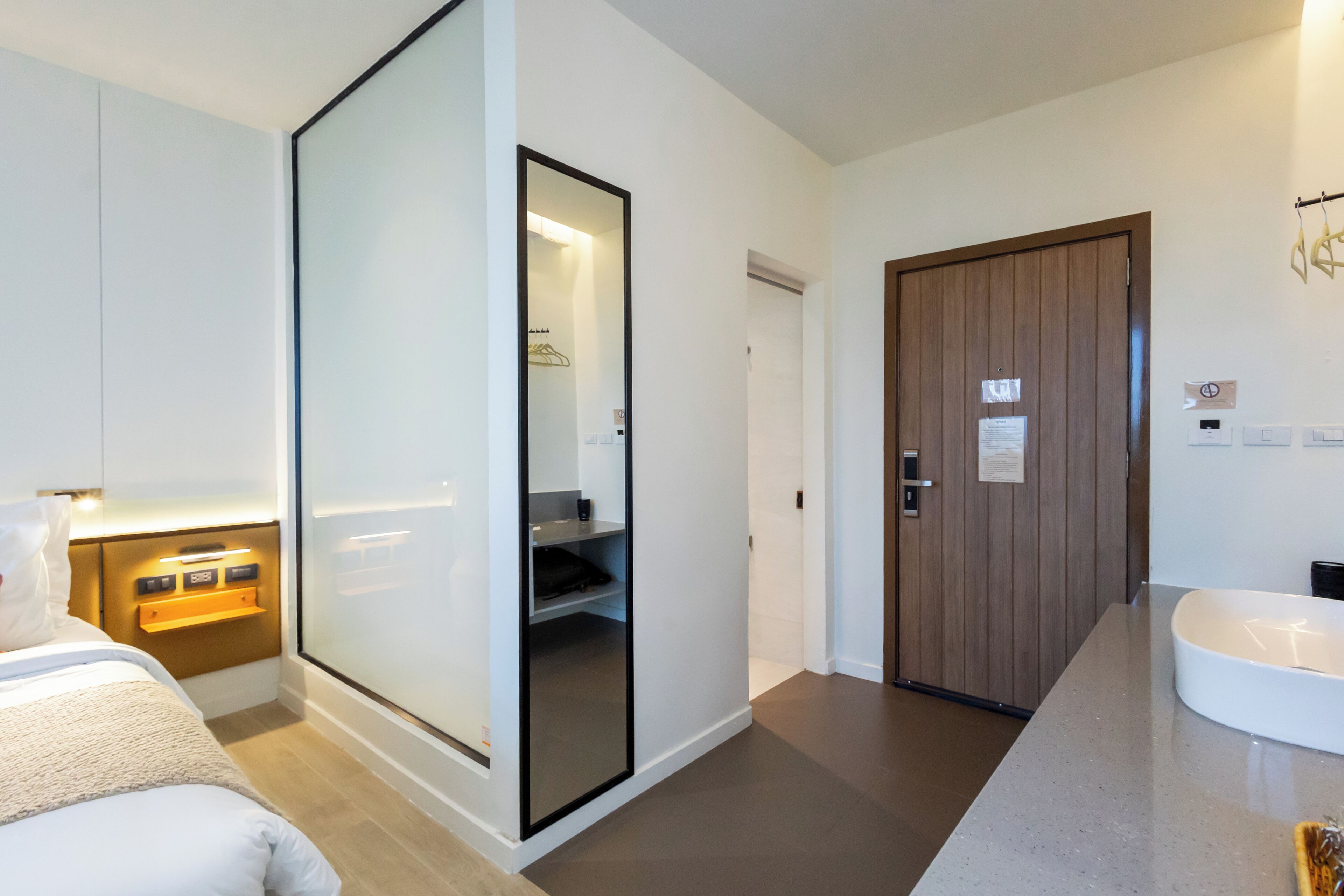 A modern hotel room with a large bed, a walk-in closet, a wooden door, and a bathroom with a white sink.