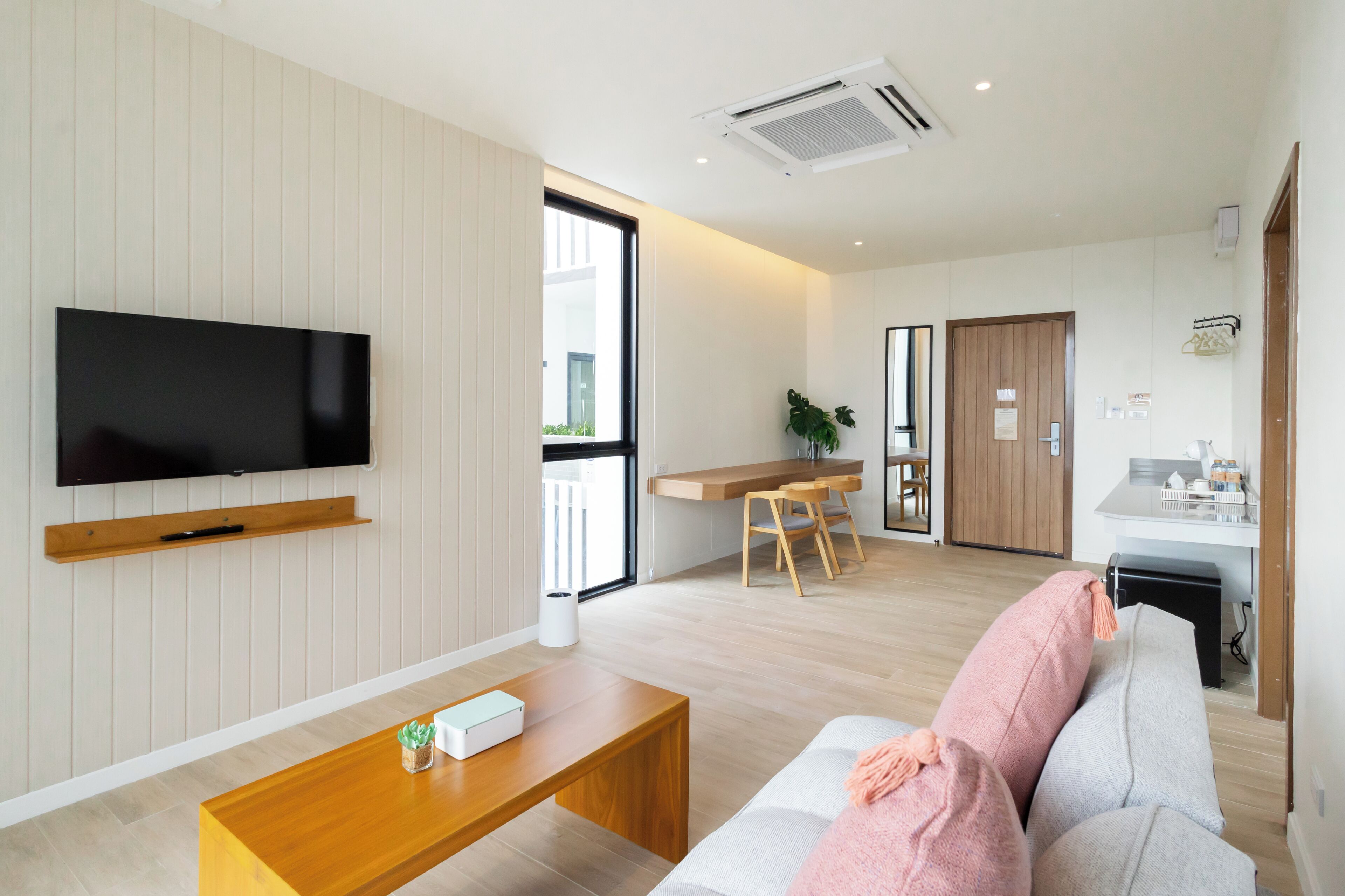 A modern living room with a flat-screen TV, wooden coffee table, and a sofa with a pink throw.