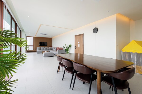 A modern dining area with a long wooden table, leather chairs, and a sofa in the background. - Good Nakhonsawan Hotel (Nakhon Sawan)