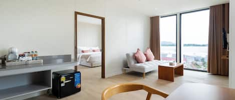 Una habitación de hotel moderna con cama, sofá, mesa de comedor y un amplio ventanal con vistas.