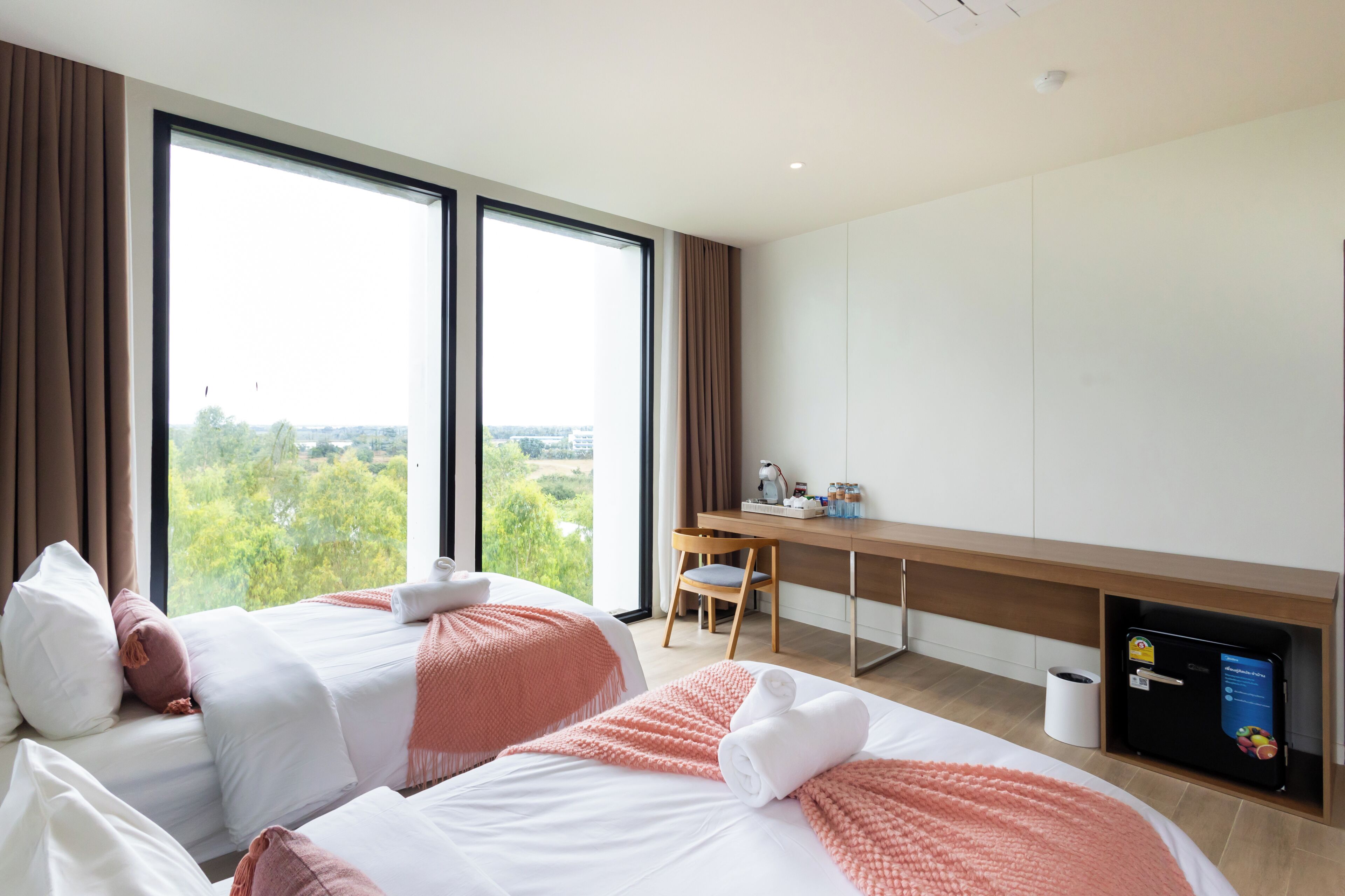 Habitación de hotel con dos camas, un escritorio y vistas a la vegetación.