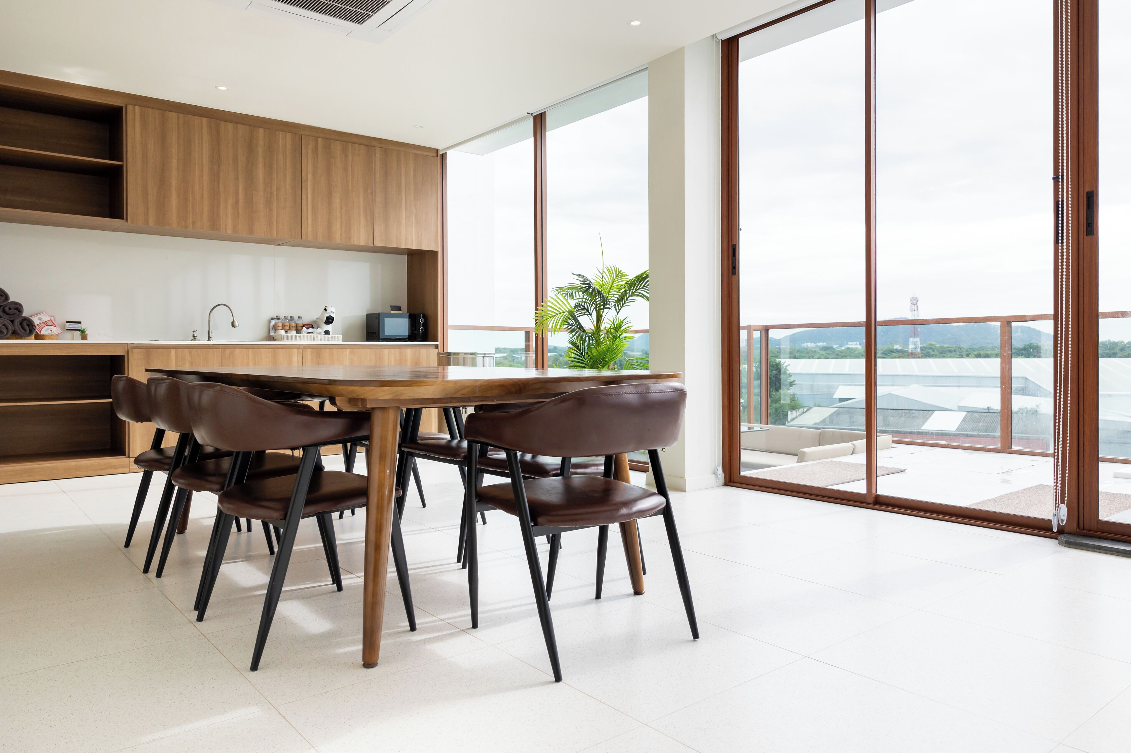 A modern kitchen with wooden cabinets, a dining table with chairs, and large windows offering a view of the cityscape.