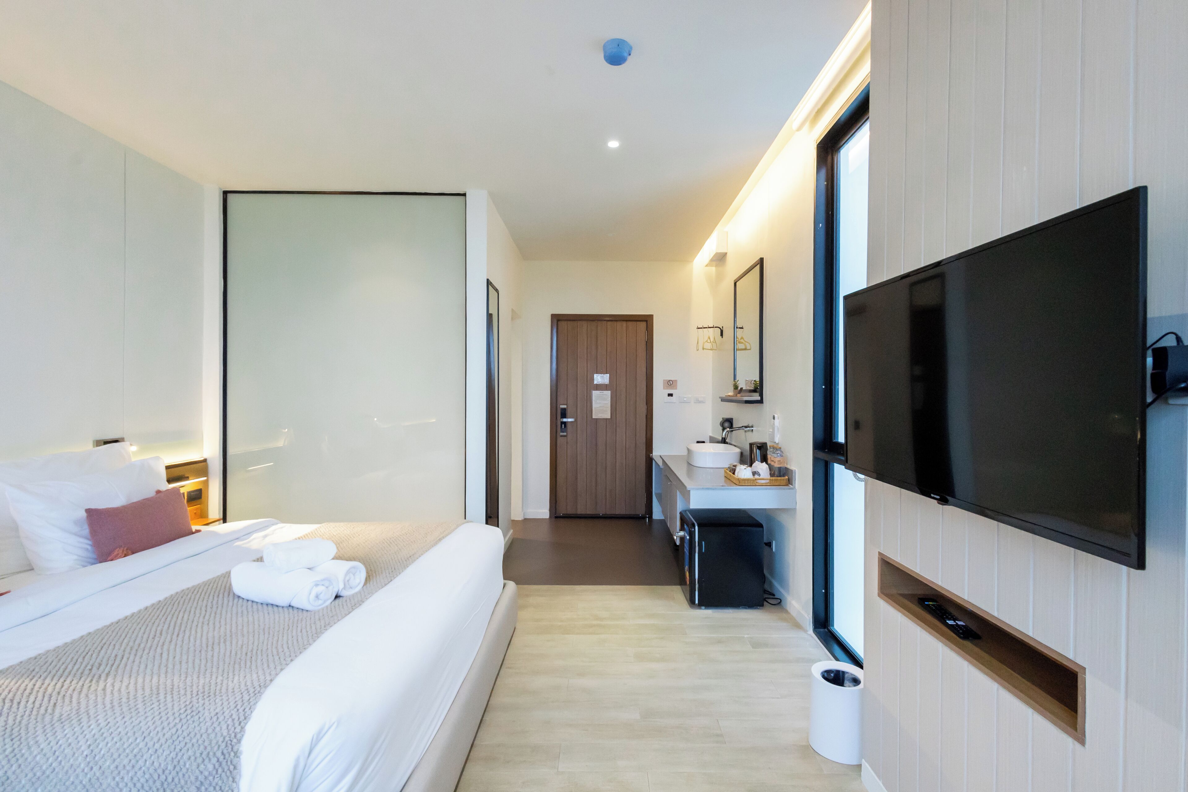 A modern hotel room with a large bed, a flat-screen TV, a small bathroom, and a wooden door.