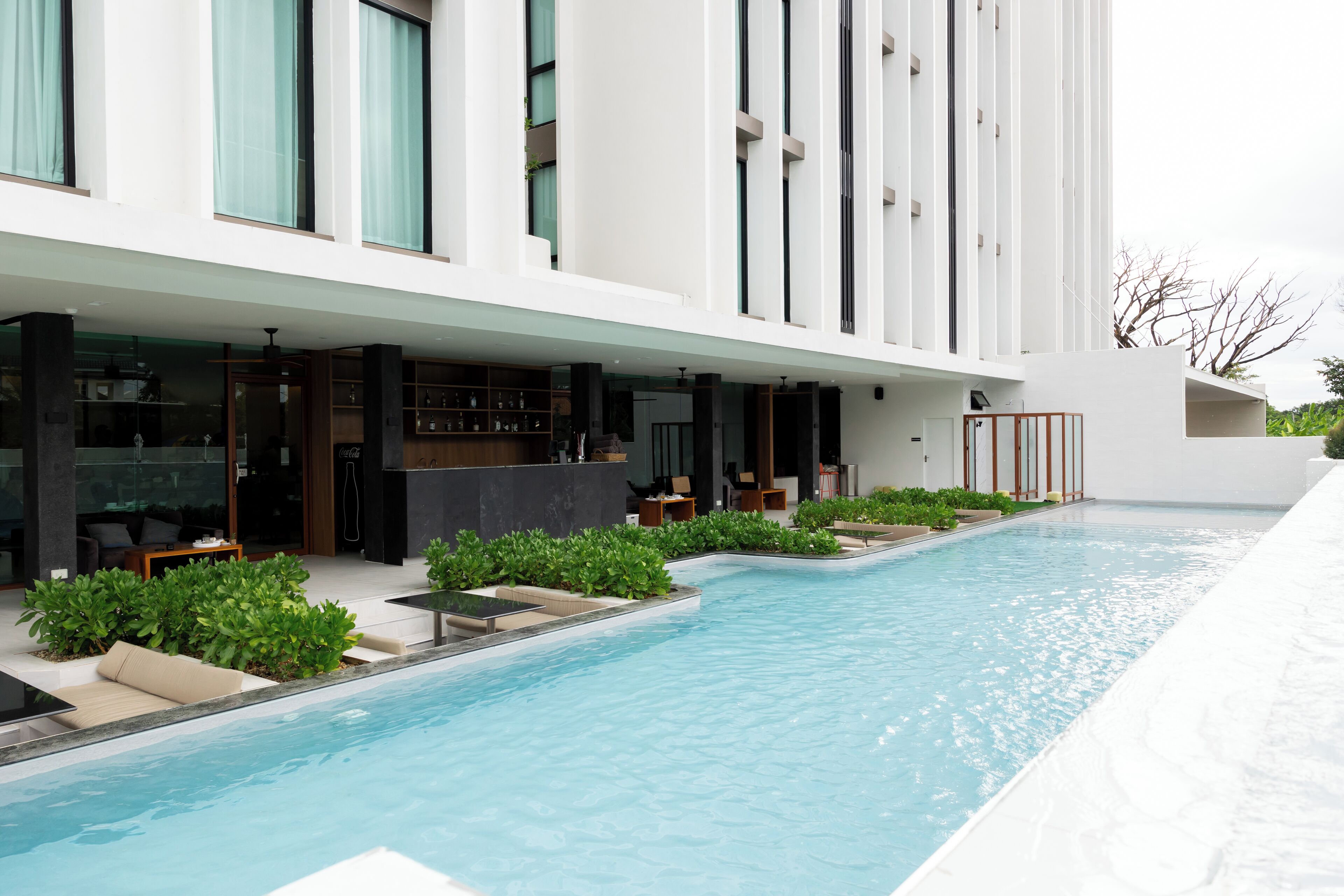 A modern building with a swimming pool, outdoor seating, and a bar area.