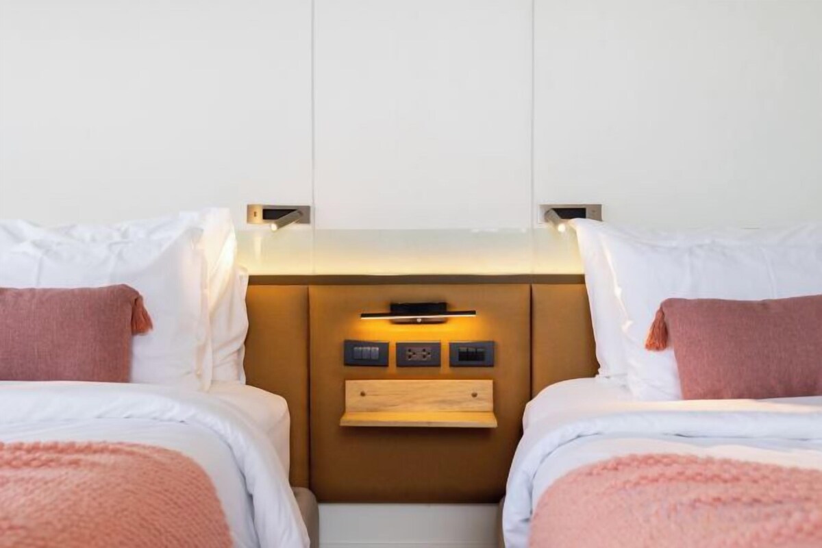 Habitación de hotel con dos camas, una mesita de noche, estante empotrado y panel de control.