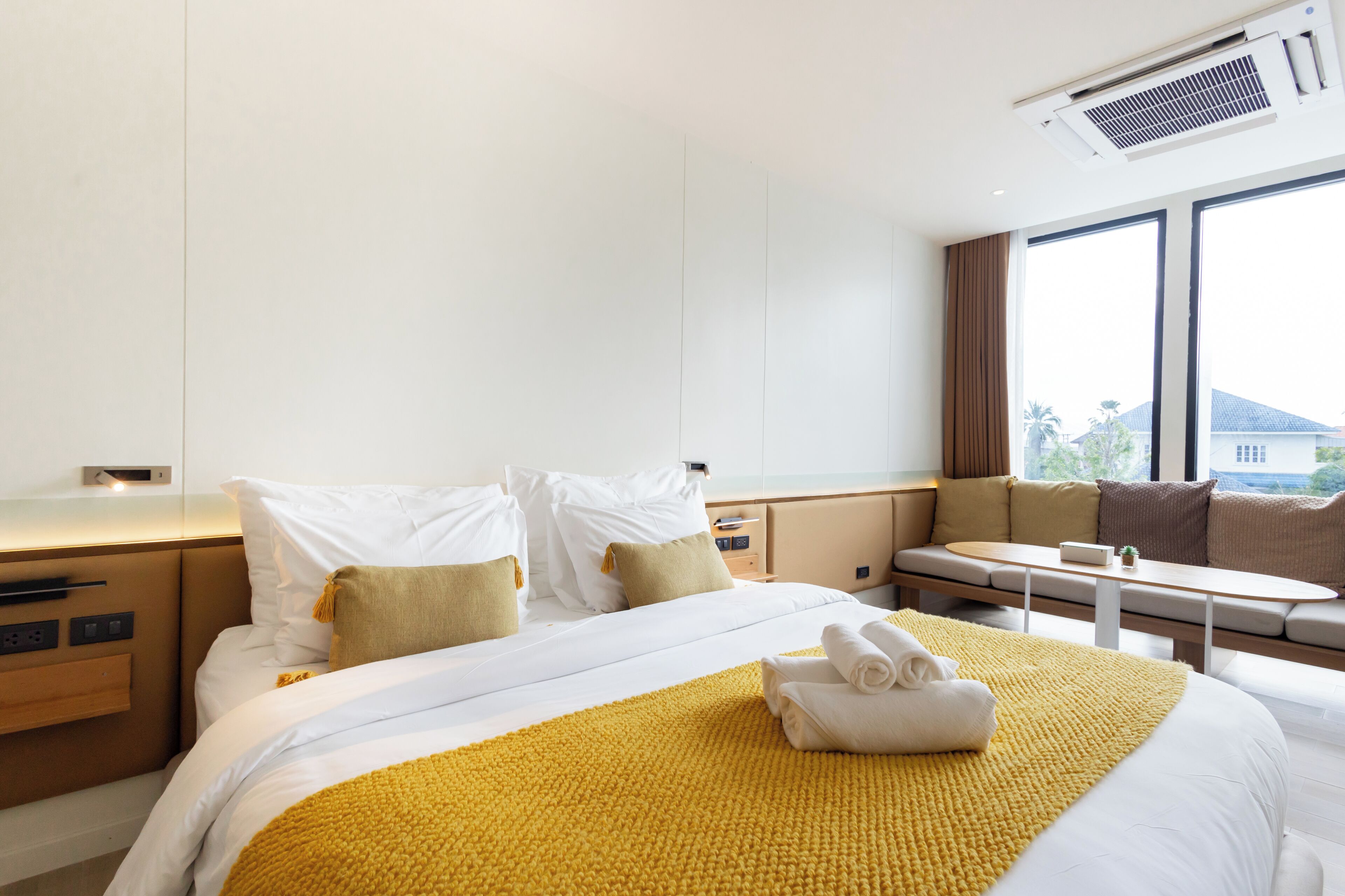 A hotel room with a large bed, a bedside table, a small table, and a sofa.