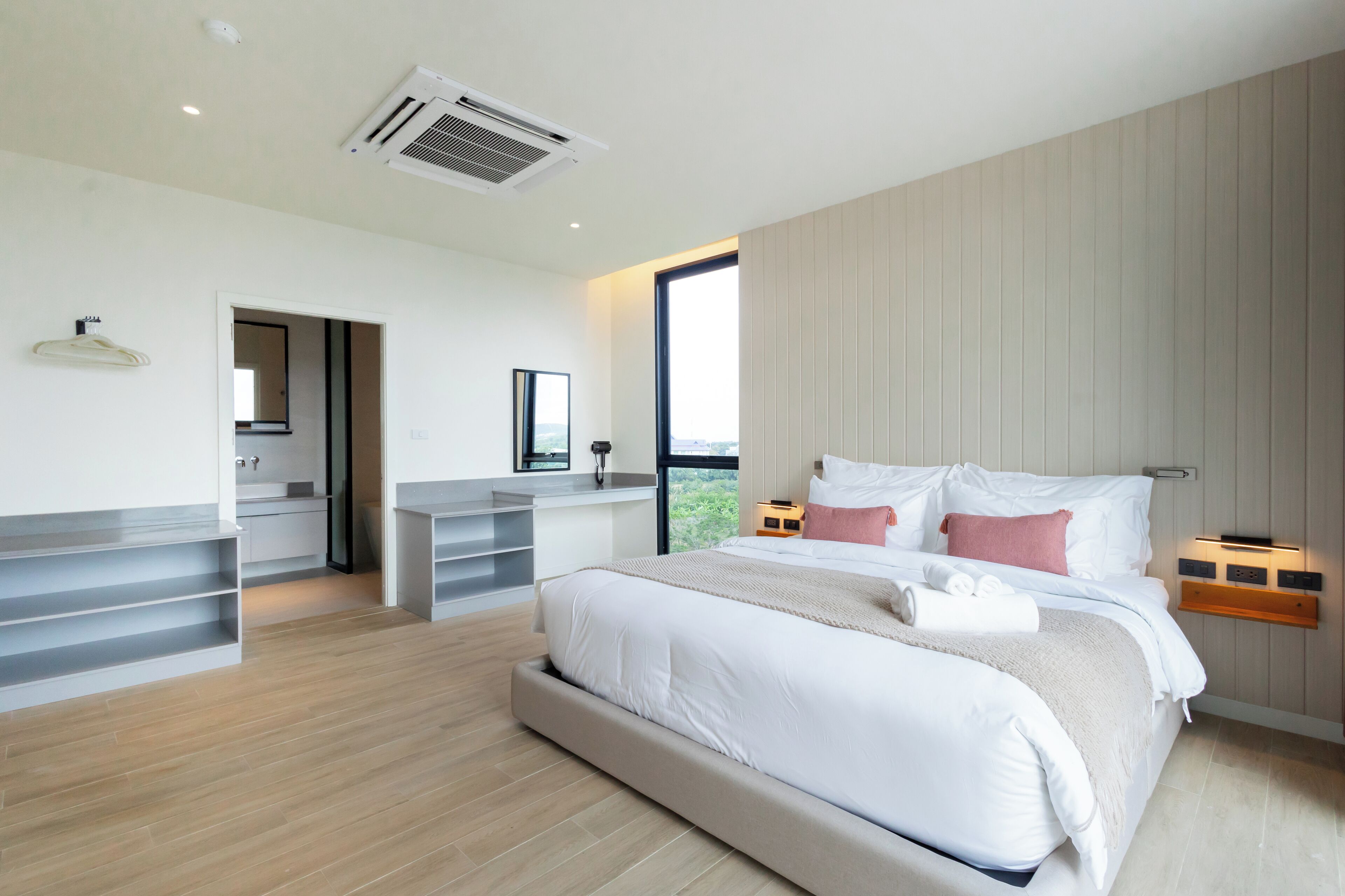 A modern bedroom with a large bed, bedside tables, a built-in desk, and a large window offering a view.