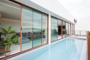 A modern hotel interior with a large glass wall, a pool, and a seating area with a view of the mountains. - Good Nakhonsawan Hotel (Nakhon Sawan)