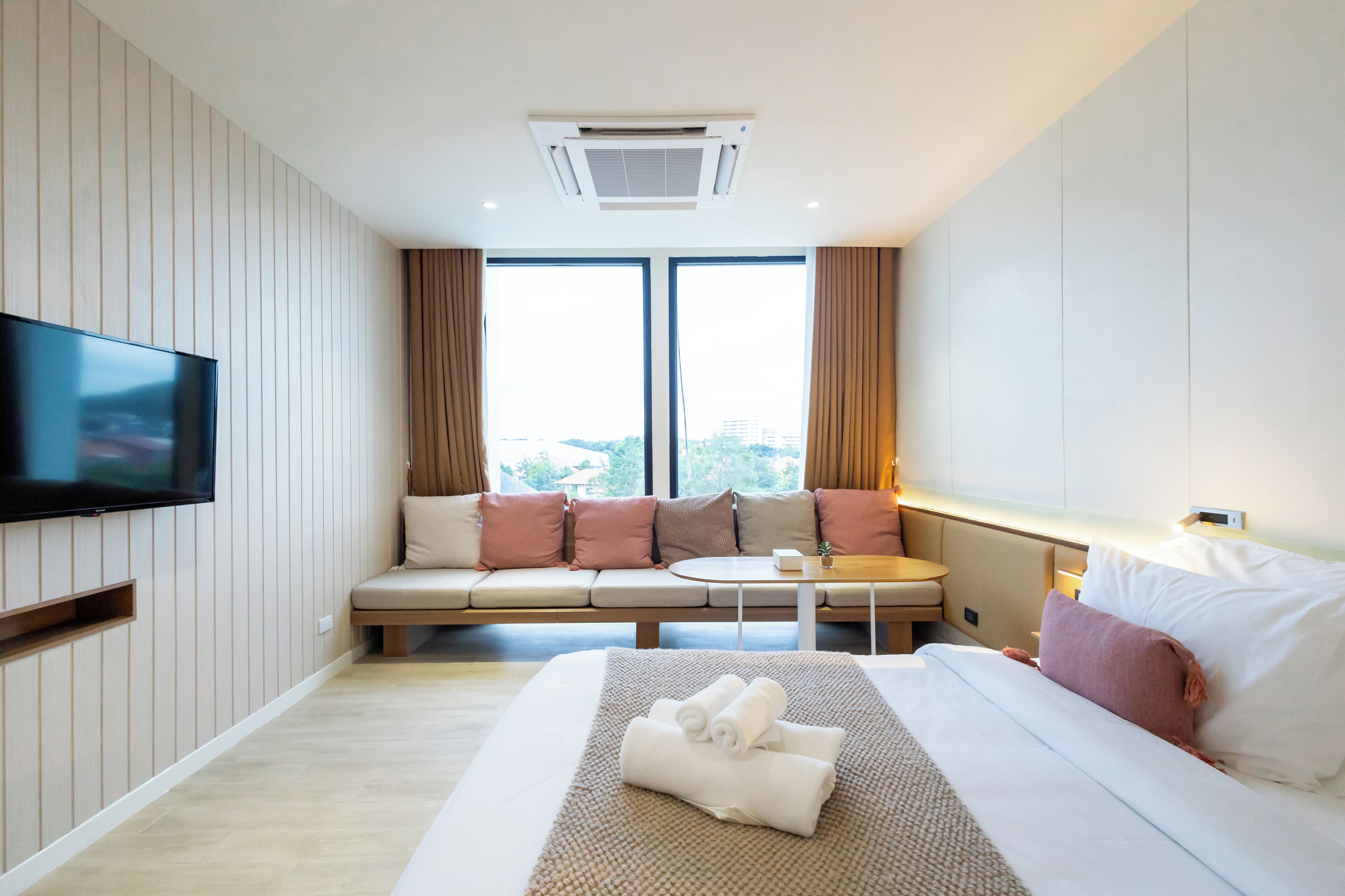 A hotel room with a bed, a TV, a sofa, and a window with curtains.