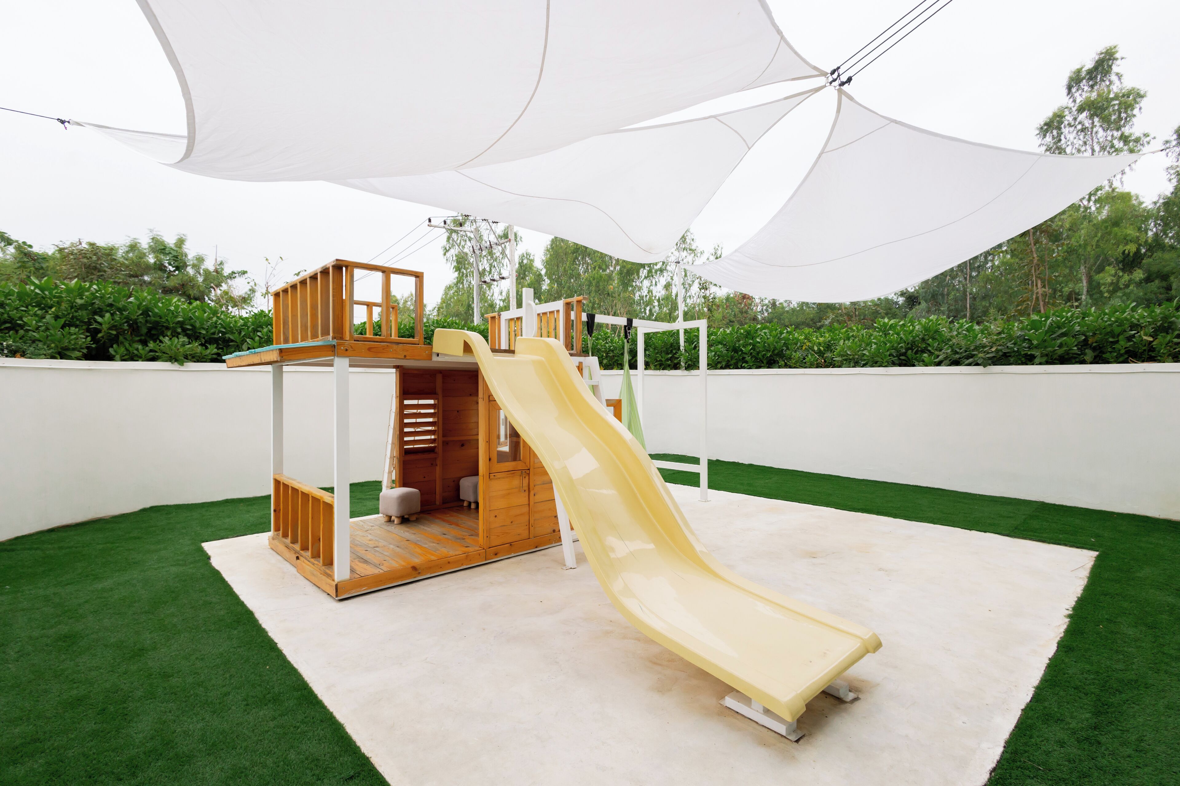 A children's play structure with a slide, surrounded by artificial grass and a white canopy.