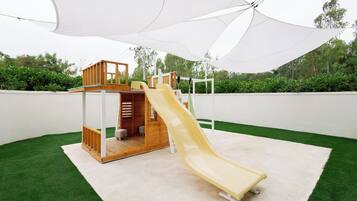 A children's play structure with a slide, surrounded by artificial grass and a white canopy.