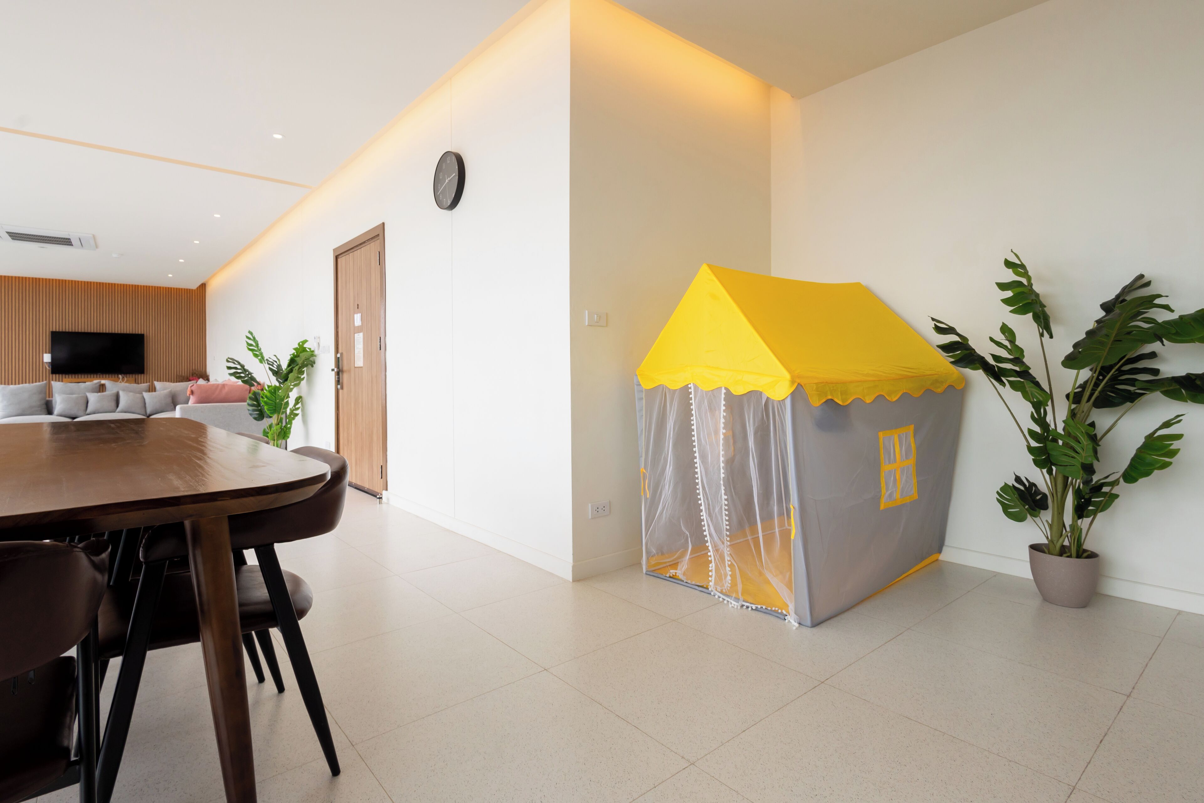 Un salon moderne avec une table à manger en bois, un canapé, un téléviseur et une petite maison de jeu jaune.