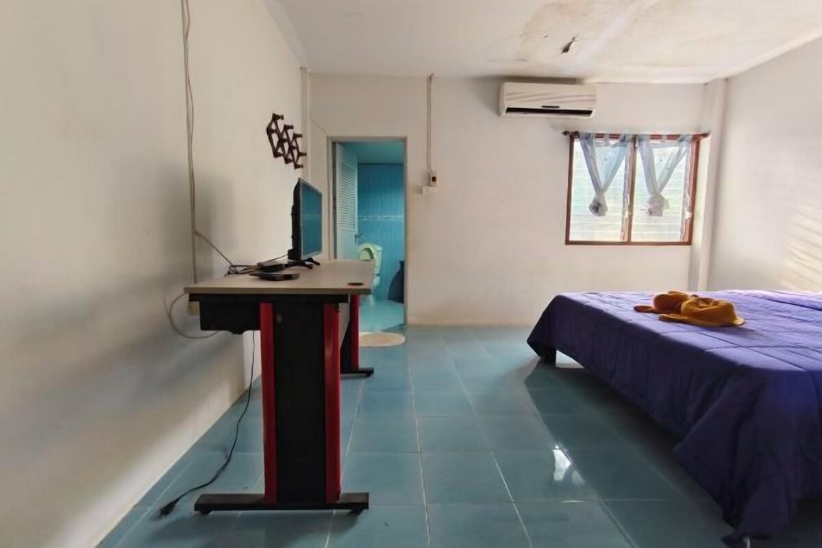 Ein Zimmer mit einem Bett, einem Schreibtisch und einem Stuhl. Es gibt ein Fenster mit Vorhängen und eine Klimaanlage an der Wand.