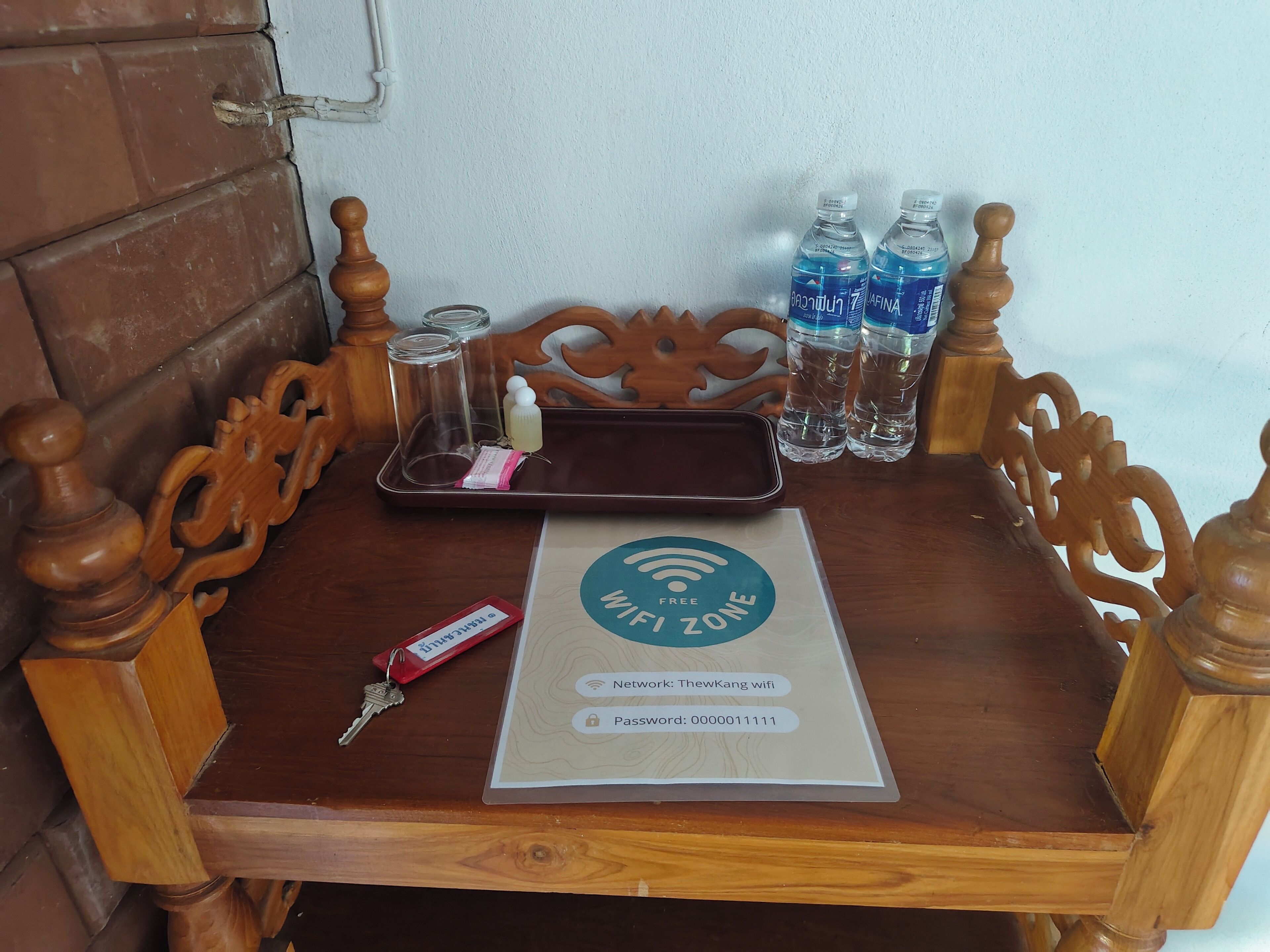 Une table en bois avec un plateau, un panneau indiquant la présence d’une connexion Wi-Fi et des bouteilles d’eau.