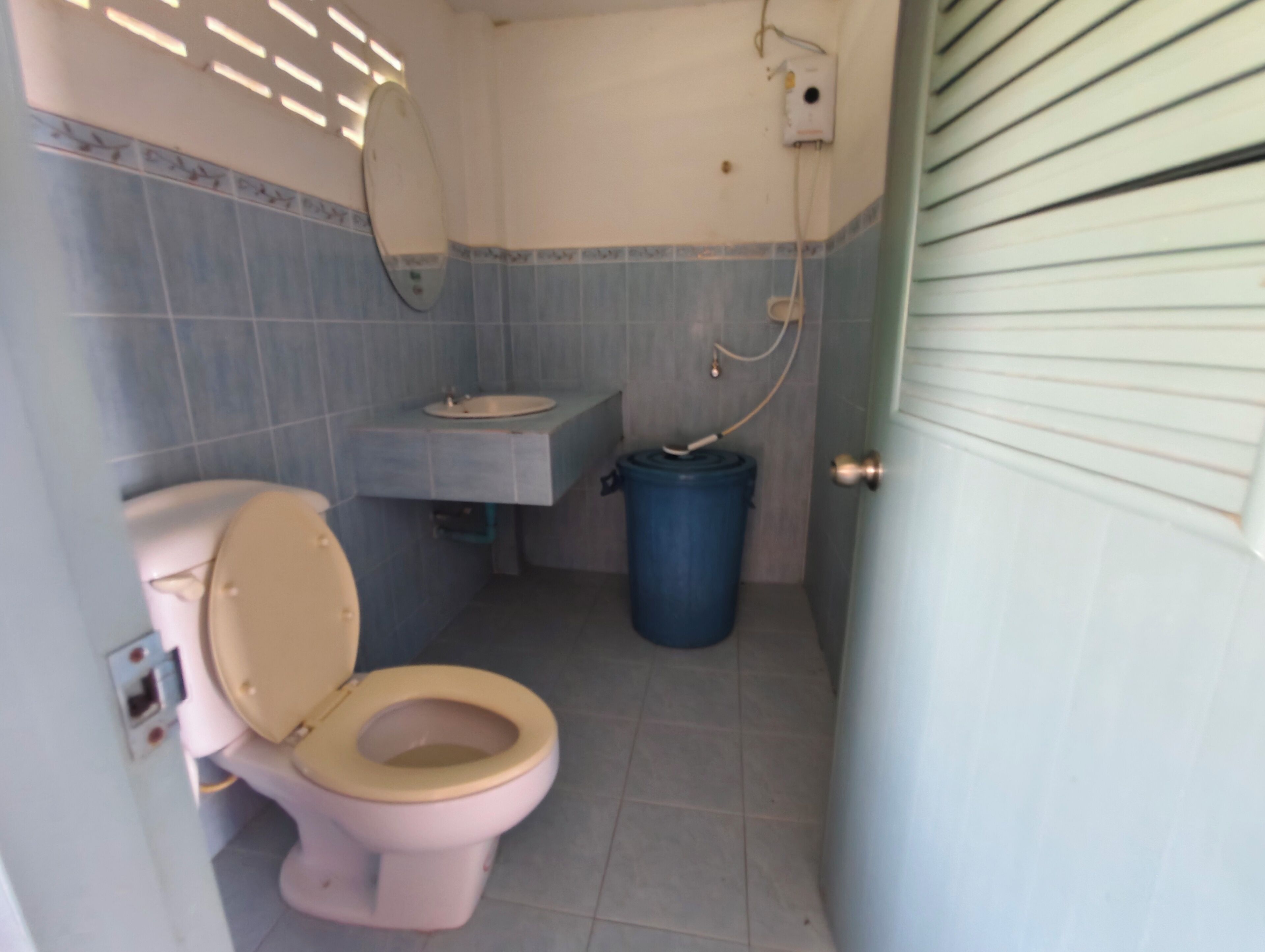 A bathroom with a toilet, sink, and blue trash bin.
