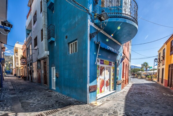 A narrow cobblestone street lined with colorful buildings, including a blue building with a balcony and a coffee shop. - Casa El Puerto by Huskalia (Tazacorte)