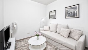 A modern living room with a sofa, two framed pictures, a small table with flowers, a TV, and a fan. - Casa El Puerto by Huskalia (Tazacorte)