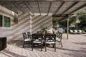 Ulkoterassi, jossa on pergola, pöytä ja tuolit sekä grillauspaikka.