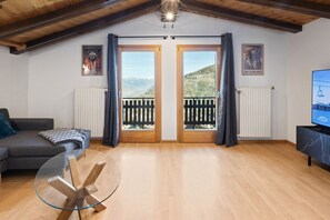 A living room with a sofa, a glass coffee table, wooden doors with a balcony, a radiator, and a television. - Modern apartment in the heart of Nendaz (Nendaz)