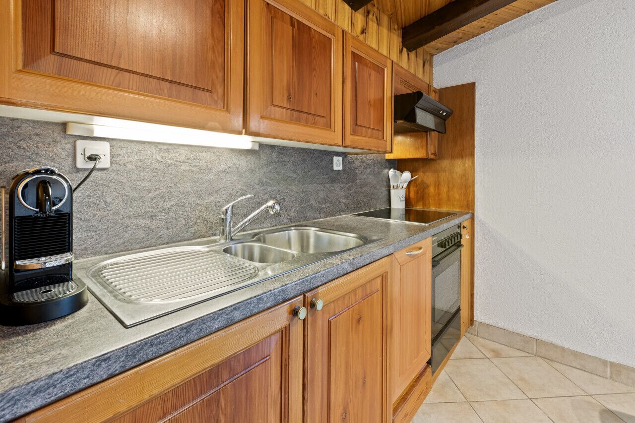 Una cocina con armarios de madera, un lavamanos de acero inoxidable, un horno empotrado y una cafetera.