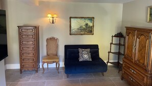 Una sala de estar con un sofá azul oscuro, un aparador de madera, una silla, una lámpara de pared y un cuadro.