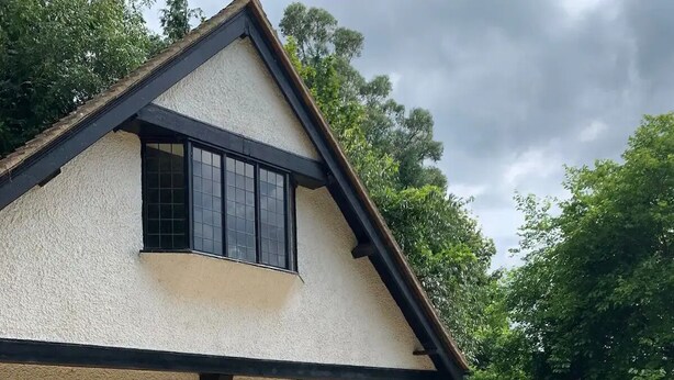Una casa de dos pisos con techo inclinado, ventanas amplias y camino de entrada de grava.