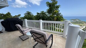 Una terrazza con due poltrone imbottite e un tavolo, che si affaccia su una vista panoramica sull'oceano e sul verde.