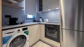 A compact kitchen with a washing machine, oven, and stainless steel refrigerator. - Phaedrus Living Athens Luxury Residences Sunstone (Athens)