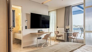A modern hotel room with a large bed, a desk with a flat-screen TV, two chairs, and a balcony with a view. - Phaedrus Living Athens Luxury Residences Sunstone (Athens)
