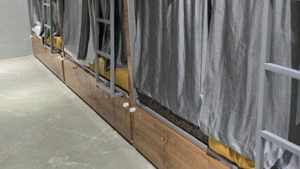 A row of bunk beds with grey curtains, wooden frames, and a tiled floor. - Classy Ac Dormitory (Mumbai)