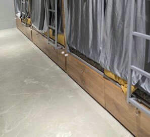 A row of bunk beds with grey curtains, wooden frames, and a tiled floor. - Classy Ac Dormitory (Mumbai)