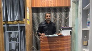 A man standing behind a wooden desk in a room with a bunk bed, a fan, and a water dispenser on the wall. - Classy Ac Dormitory (Mumbai)