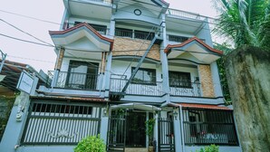 A multi-story residential building with balconies, a gated entrance, and a stone wall. - Hymn's Tourist Inn (Coron)