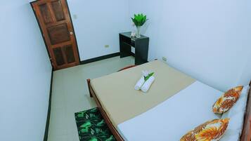 Un dormitorio pequeño y ordenado con cama, mesita de noche con una planta y una puerta.