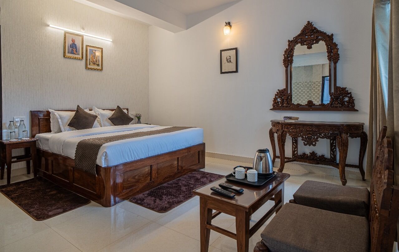 A hotel room with a large bed, bedside tables, a wooden dresser, a mirror, and a seating area.