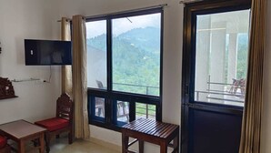 A room with a large window offering a view of hills, a television mounted on the wall, a wooden table, and a chair. - Captain Resort (Kasauli)