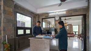 A reception area with a stone wall, a reception desk, and a view into a living area with a sofa and a dining table. - Captain Resort (Kasauli)