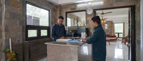 A reception area with a stone wall, a reception desk, and a view into a living area with a sofa and a dining table.