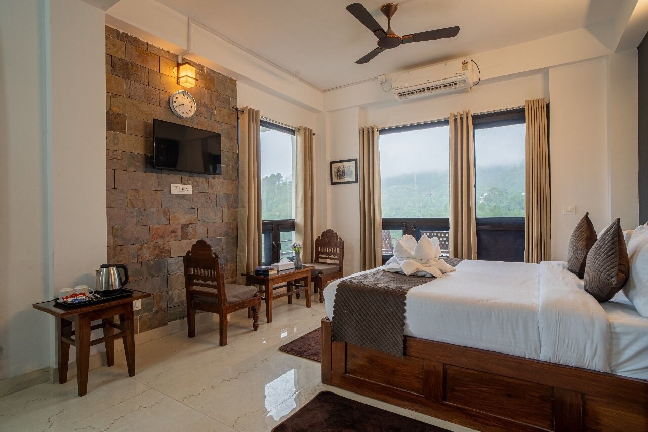 A bedroom with a stone wall, a bed, a desk, a chair, a television, and a view of the outdoors.