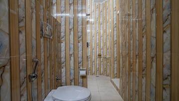 Un baño con pared de mármol, inodoro y zona de ducha.