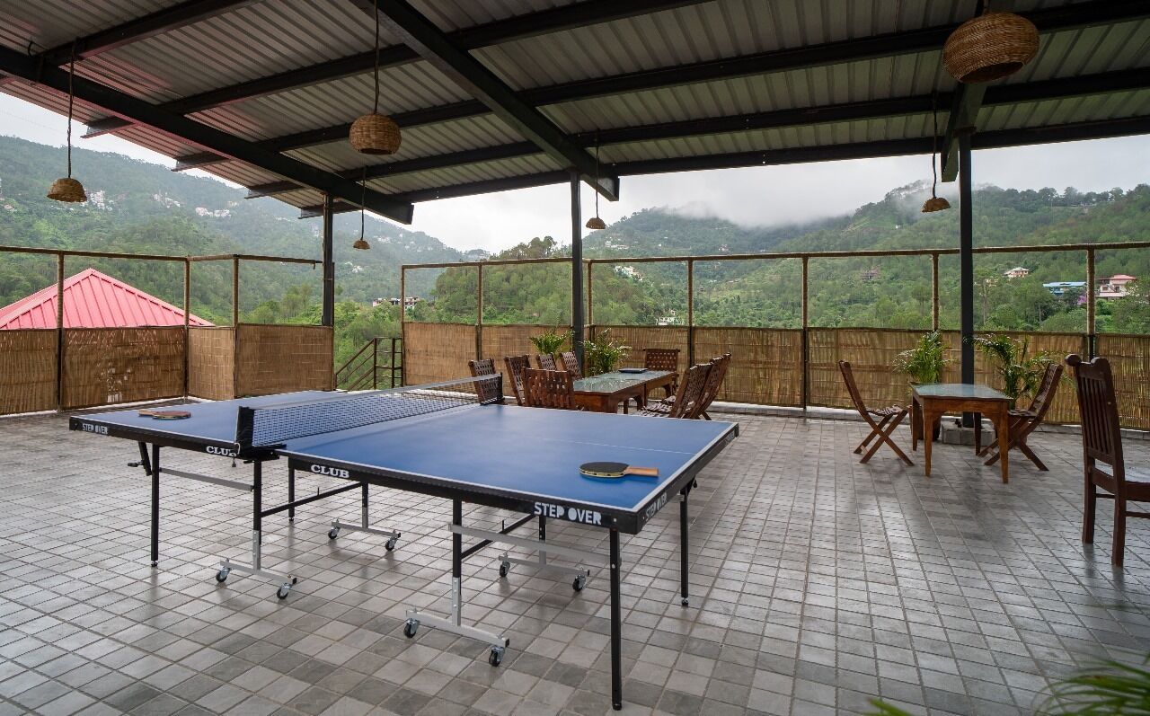 Una mesa de ping pong montada en un patio con baldosas, con sillas y mesas, con vistas a un paisaje montañoso.